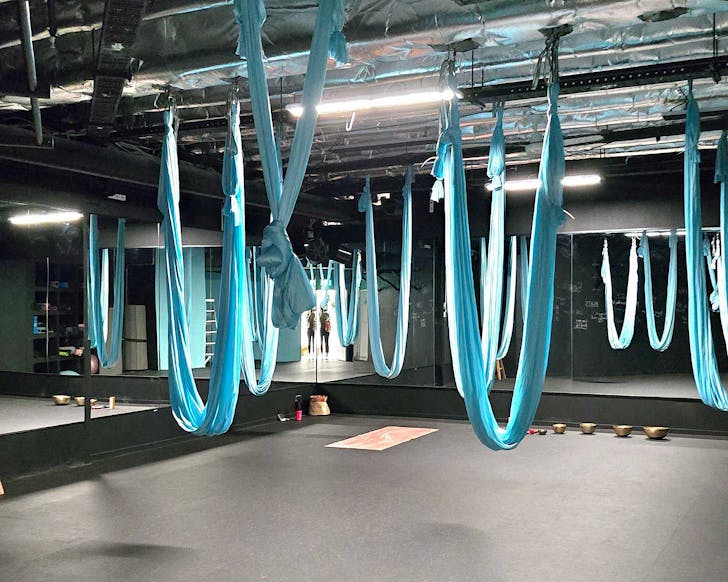 A black yoga studio with light blue silk yoga hammocks hanging from the ceiling. 