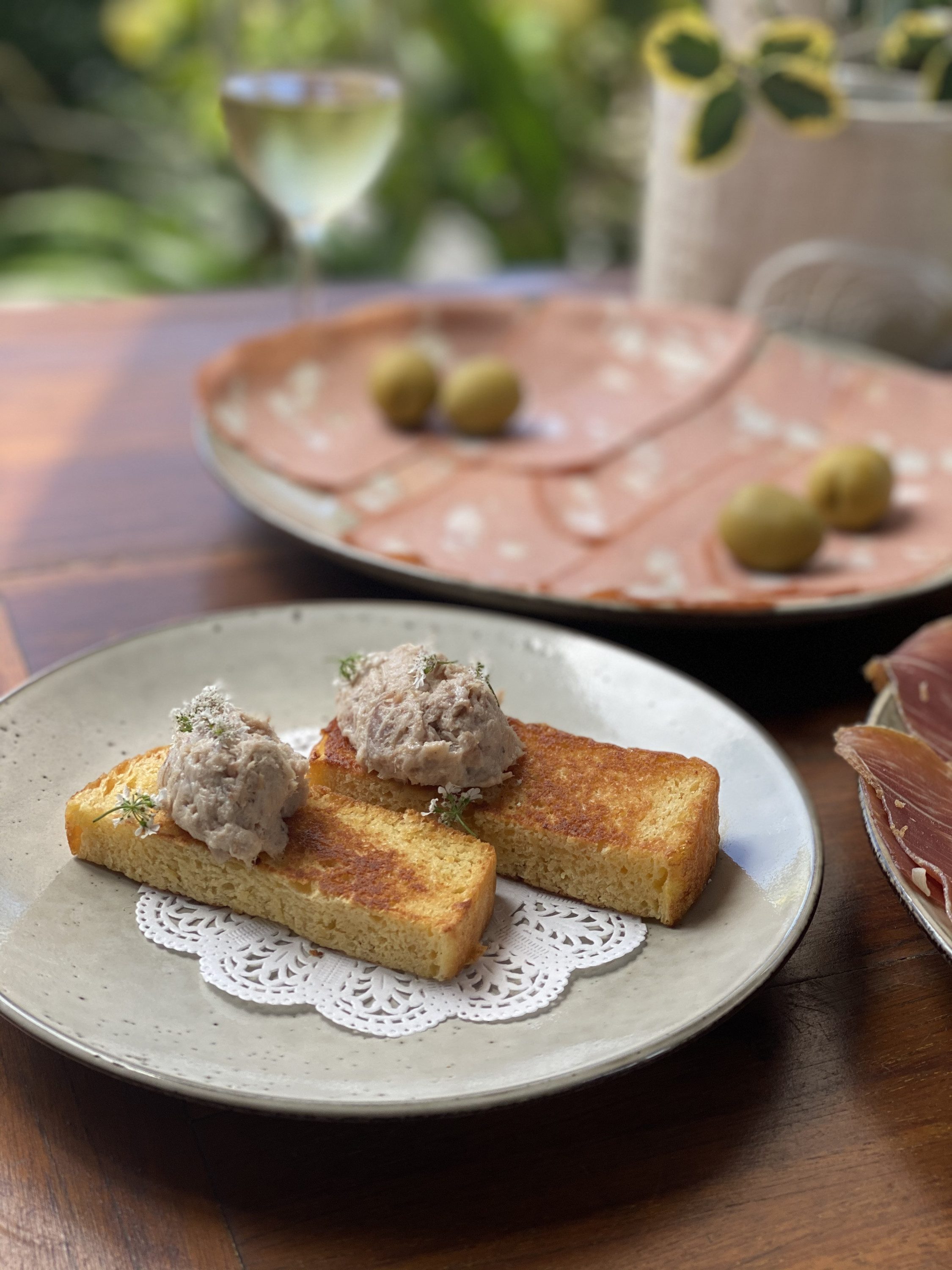 a pork rilette dish with a wine glass in the background