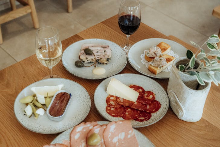 a table full of various plates with salumi and aperitivo dishes with a glass of wine
