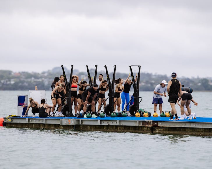 A group of fitness influencers smash a hyrox-inspired ski erg challenge on a floating blue astroturfed pontoon. 