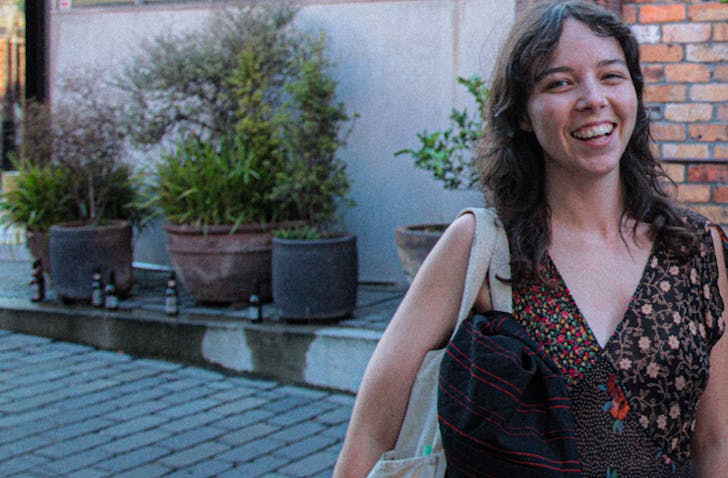 Hannah of Dangerous Goods stands smiling in front of a plants and shrubs