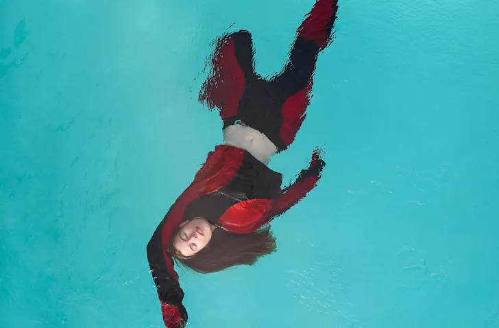 Hannah Lee Jade floats in a swimming pool wearing black and red threads. 