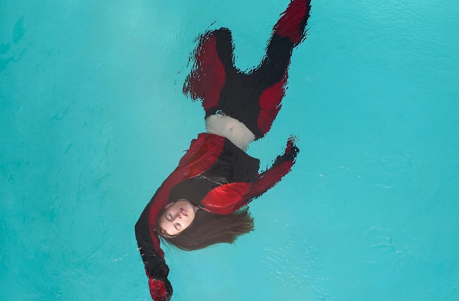 Hannah Lee Jade floats in a swimming pool wearing black and red threads. 