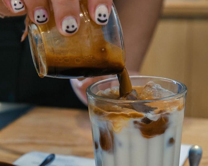 A barista with smiley face nails pours a coffee at Akin Cafe, one of the best cafes in Christchurch. 