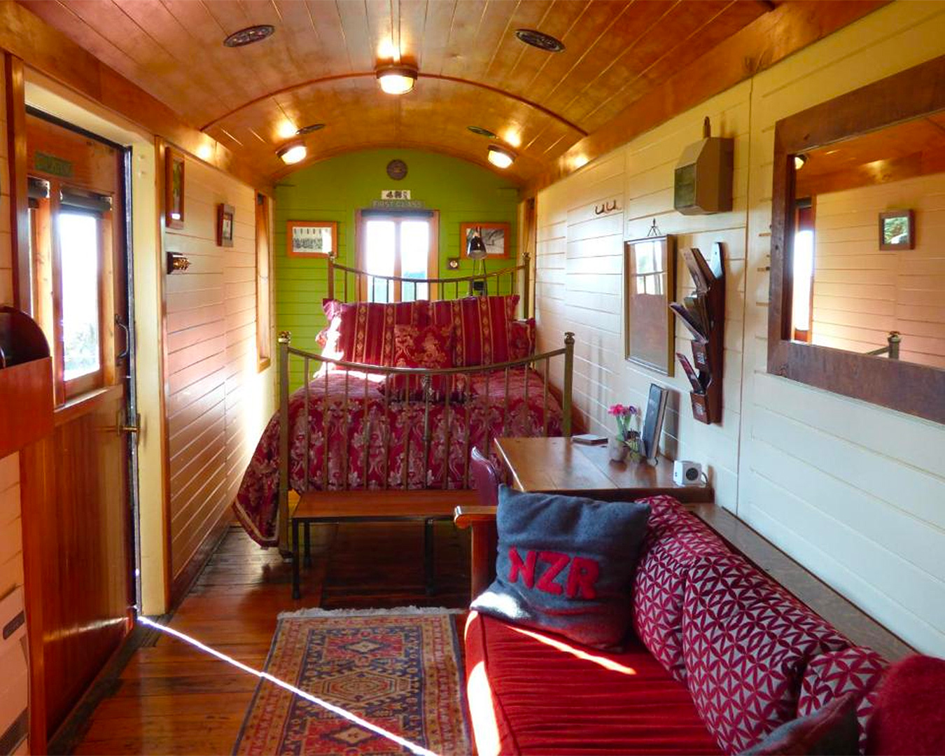 A cosy bed with red patterned bedspread awaits within a restored railway carriage. 