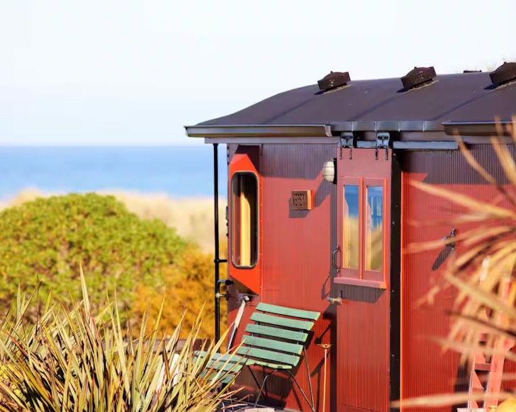 A view of the red exterior of Hapuku Carriages cosy cabin in New Zealand