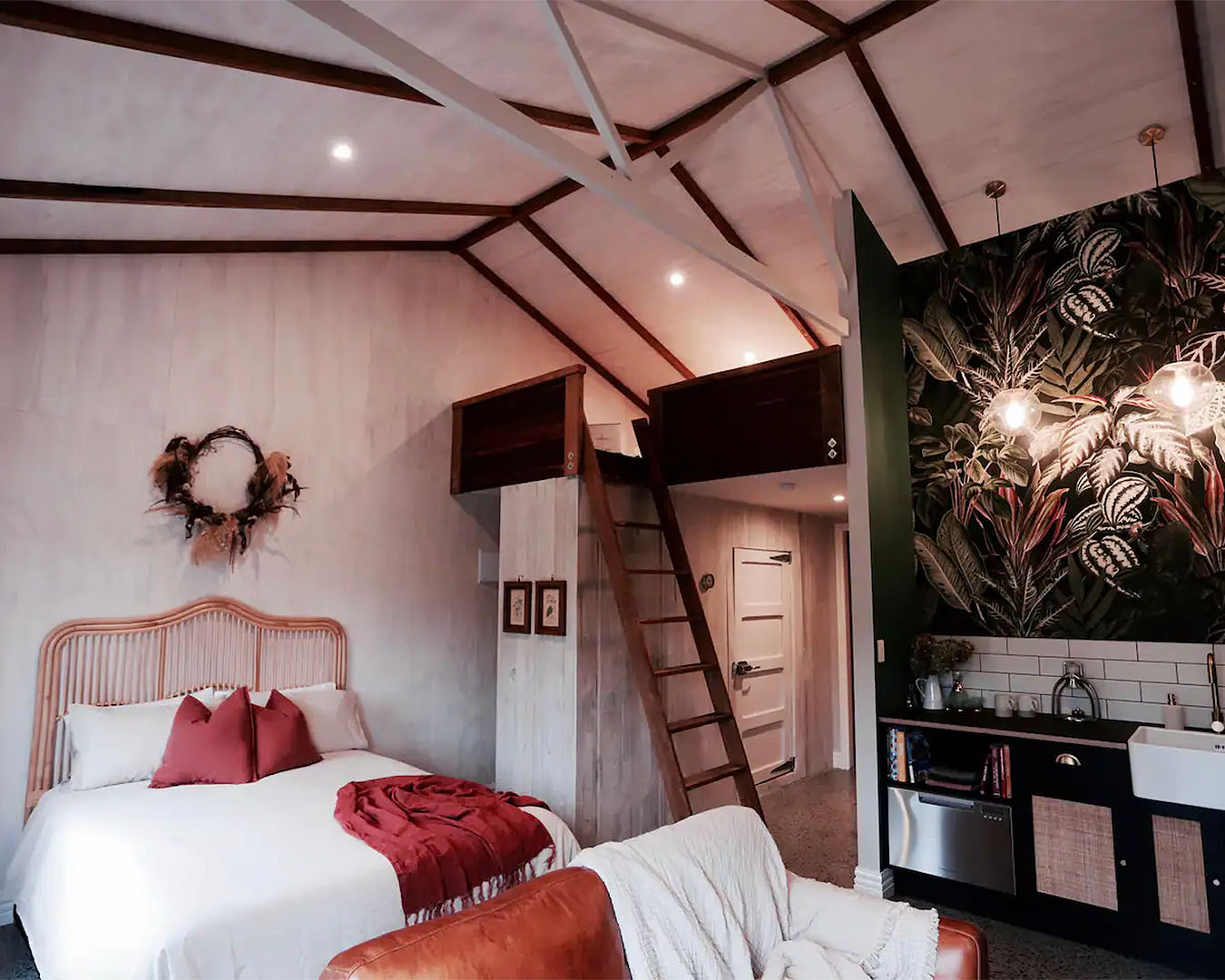 A comfortable room with wooden beams, a cosy bed, art on the wall and a little kitchenette at Harewood Grange, one of the best airbnbs in NZ with a fireplace.