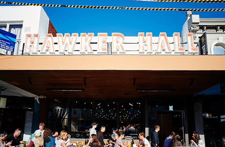People dining in front of Hawker Hall. The sun shines above the restaurant.