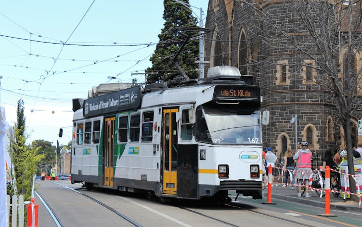 A tram going up a road with people walking alongside it. 