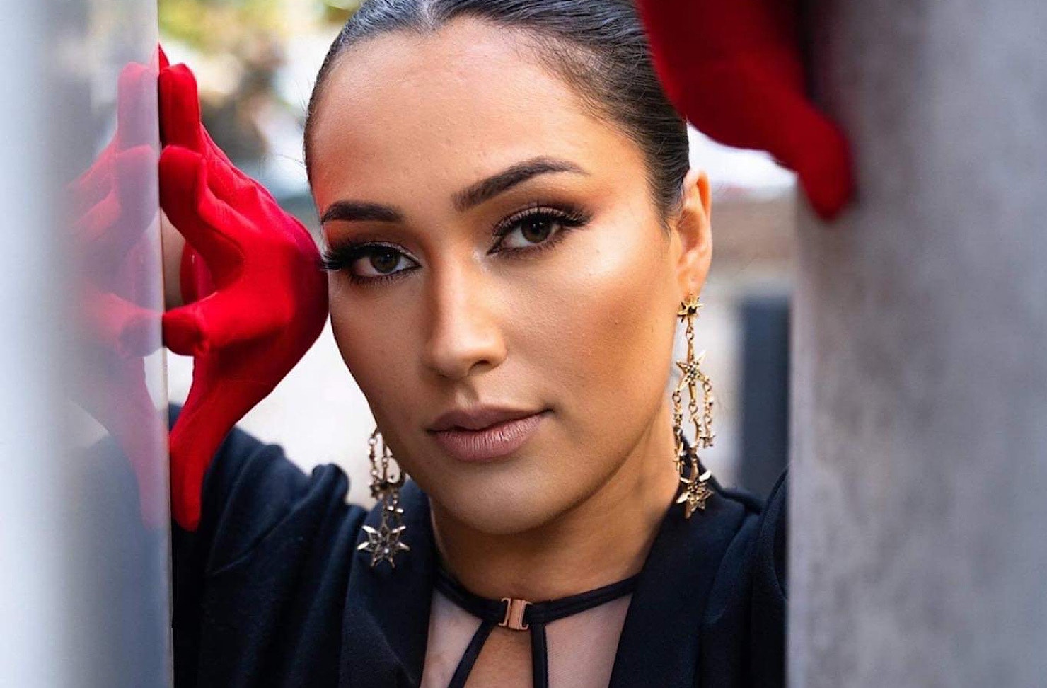 Hayley Tekahika poses between architecture, wearing striking red gloves and an ornate black top. 