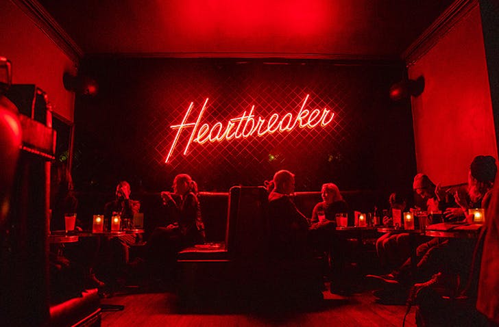 A bright neon sign reads Heartbreaker illuminates a dark room at one of the best bars in Melbourne