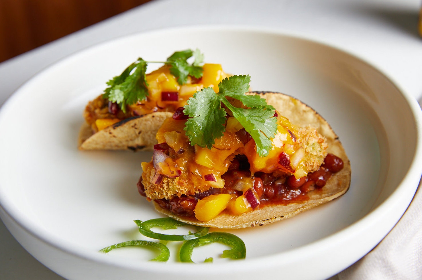 Two crispy avo tacos sit on a plate topped with mango salsa.