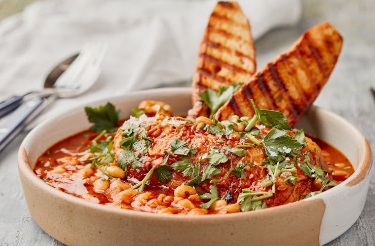 A hearty chicken cassoulet dish is topped with baked beans, bread and parsley. 