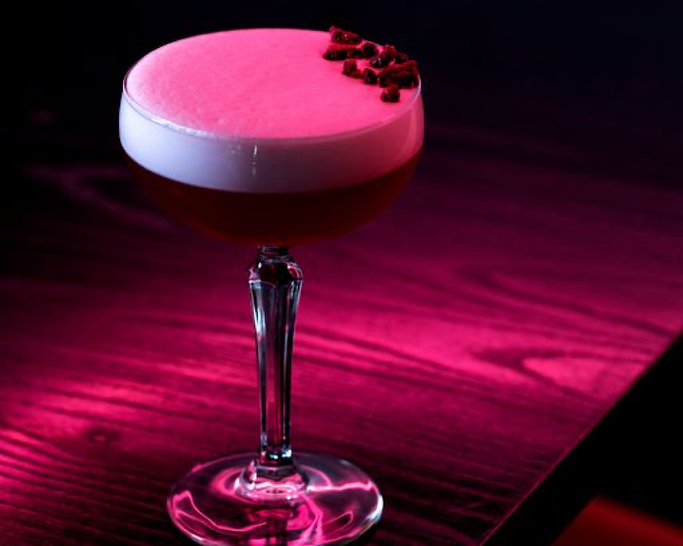 A red-lit martini glass holds a red cocktail with a thick foam top studded with fruit gems at Hello Beasty. 