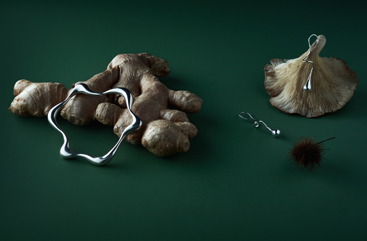 A piece of Hera Saabi jewellery lays on top of a piece of ginger, both against a green backdrop
