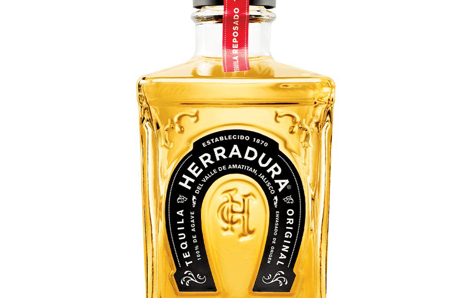 A bottle of tequila with a amber liquid and gold and black lettering.