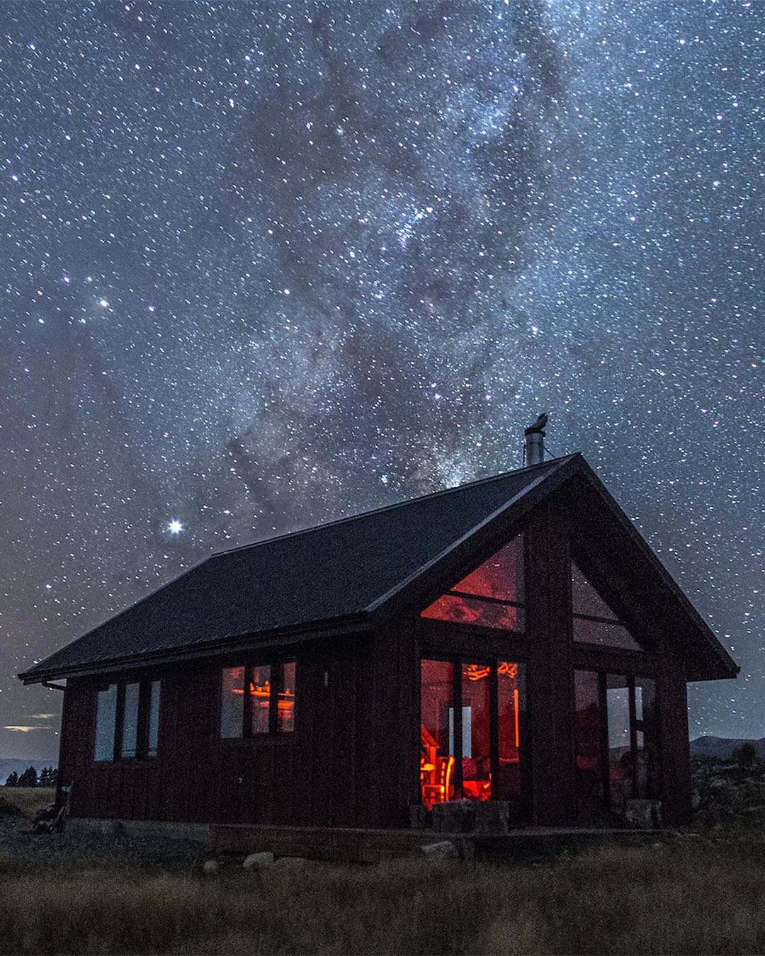 The gorgeous high country cabin is seen from the outside on an impossibly starry night. One of the best airbnbs with fireplaces in the south island.