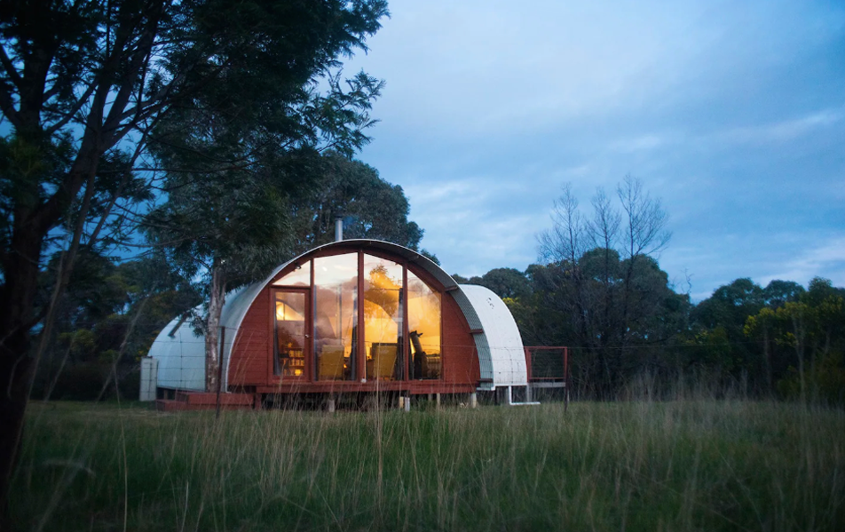 A rounded house with large glass windows with the lights on at one of the best romantic getaways in Victoria.