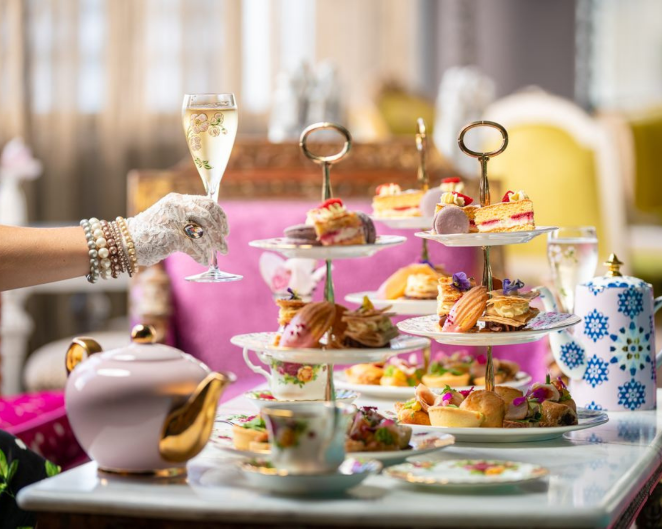 A lady holding a glass of bubbles next to a beautiful display of food and beverages at a high tea