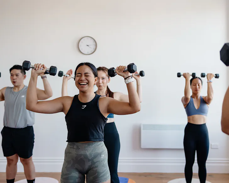 A group of people breathe and laugh while they hold dumbbells in a mat pilates class. 