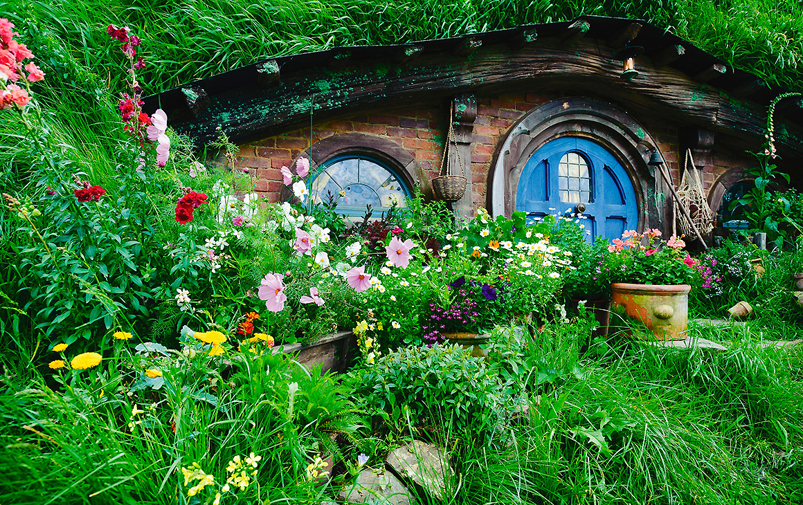 A hidden doorway surrounded by lush green vegetation and flowers at Hobbiton, one of New Zealand's top tourist attractions.