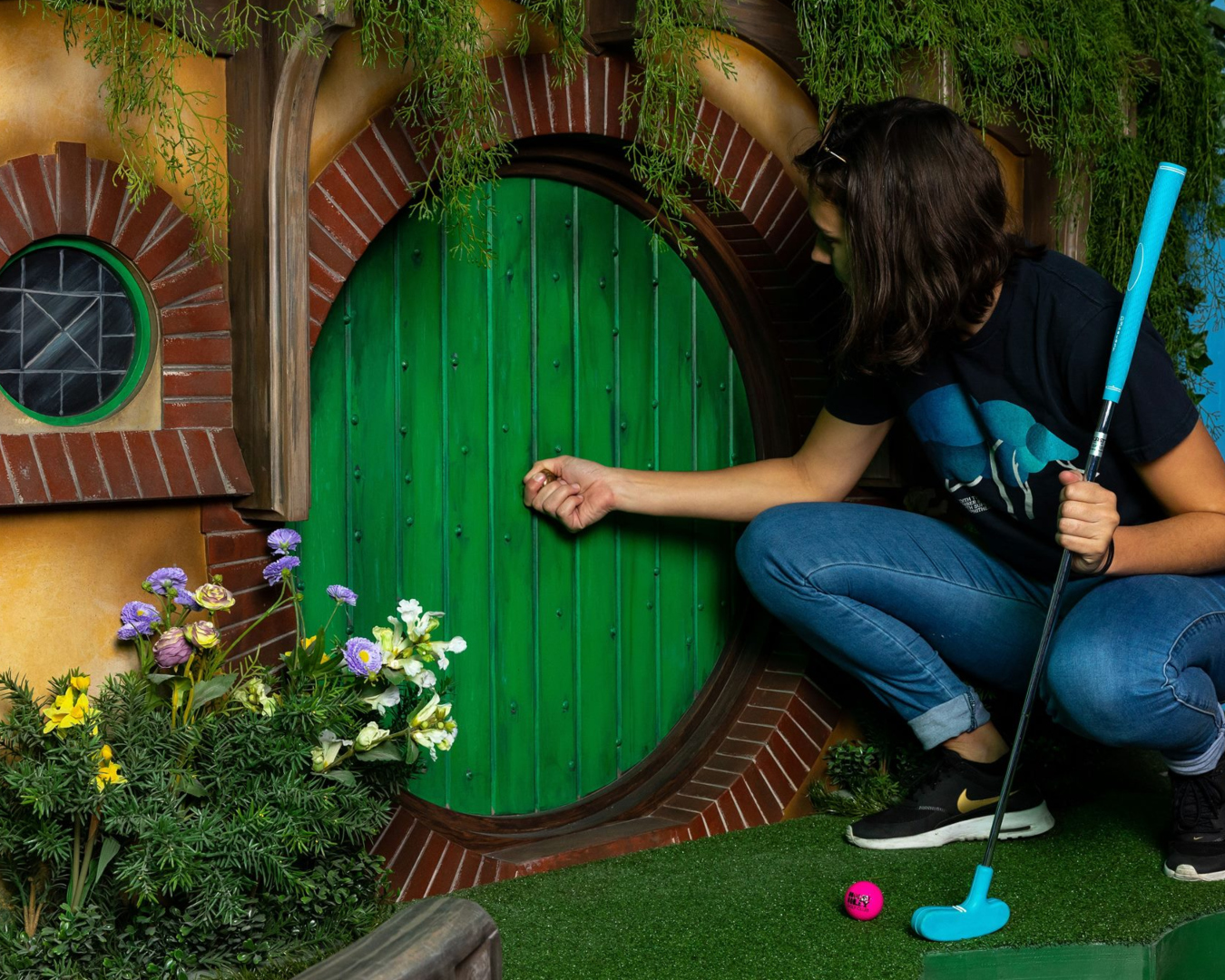 A person opens a small green door while holding a putt at one of the best mini-golf courses in Auckland.