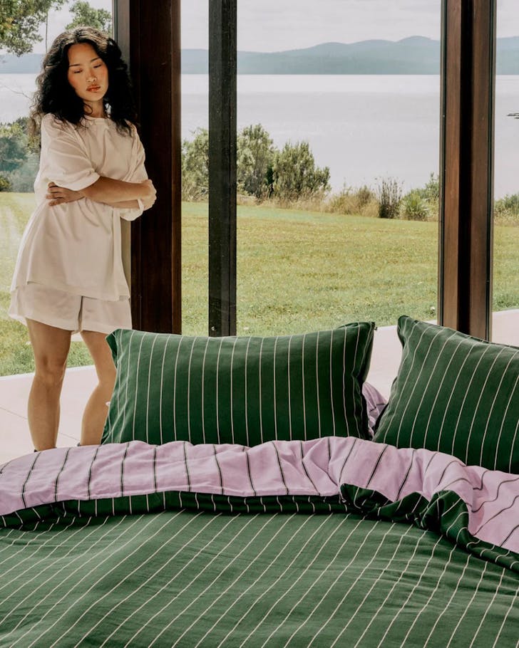 A woman stands next to a bed with a Hommey quilt in green stripe