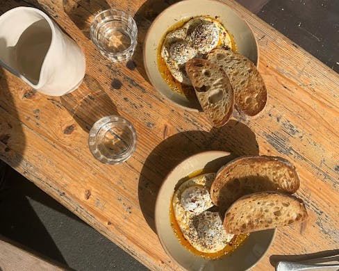 Two bowls of Cilbir eggs with sourdough. 