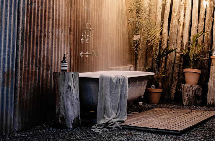 A free-standing bathtub sits outside with a rain shower above.