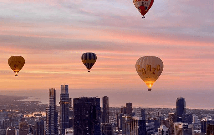 A group of hot air balloons soaring above Melbourne CBD at sunrise. 