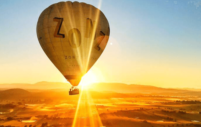 A large yellow hot air balloon Yarra Valley experience with the sun rising.