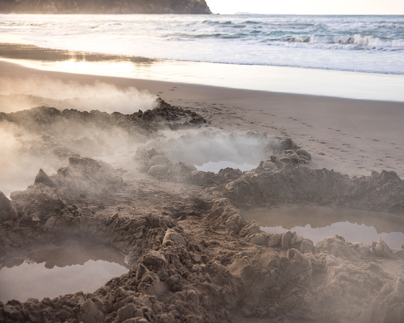 Steam rising from freshly-dug natural sand spa pools on Hot Water Beach, one of the best hidden beaches in New Zealand. 