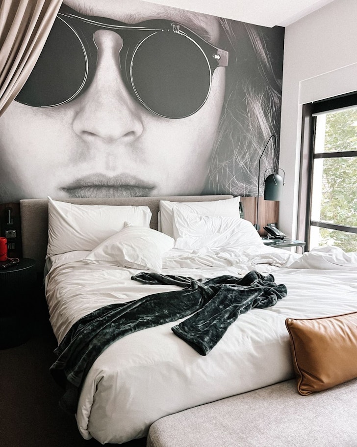 A view of a bed in front of wallpaper showing a woman's face at Hotel Indigo Melbourne On Flinders one of the best hotels for British and Irish Lions Tour