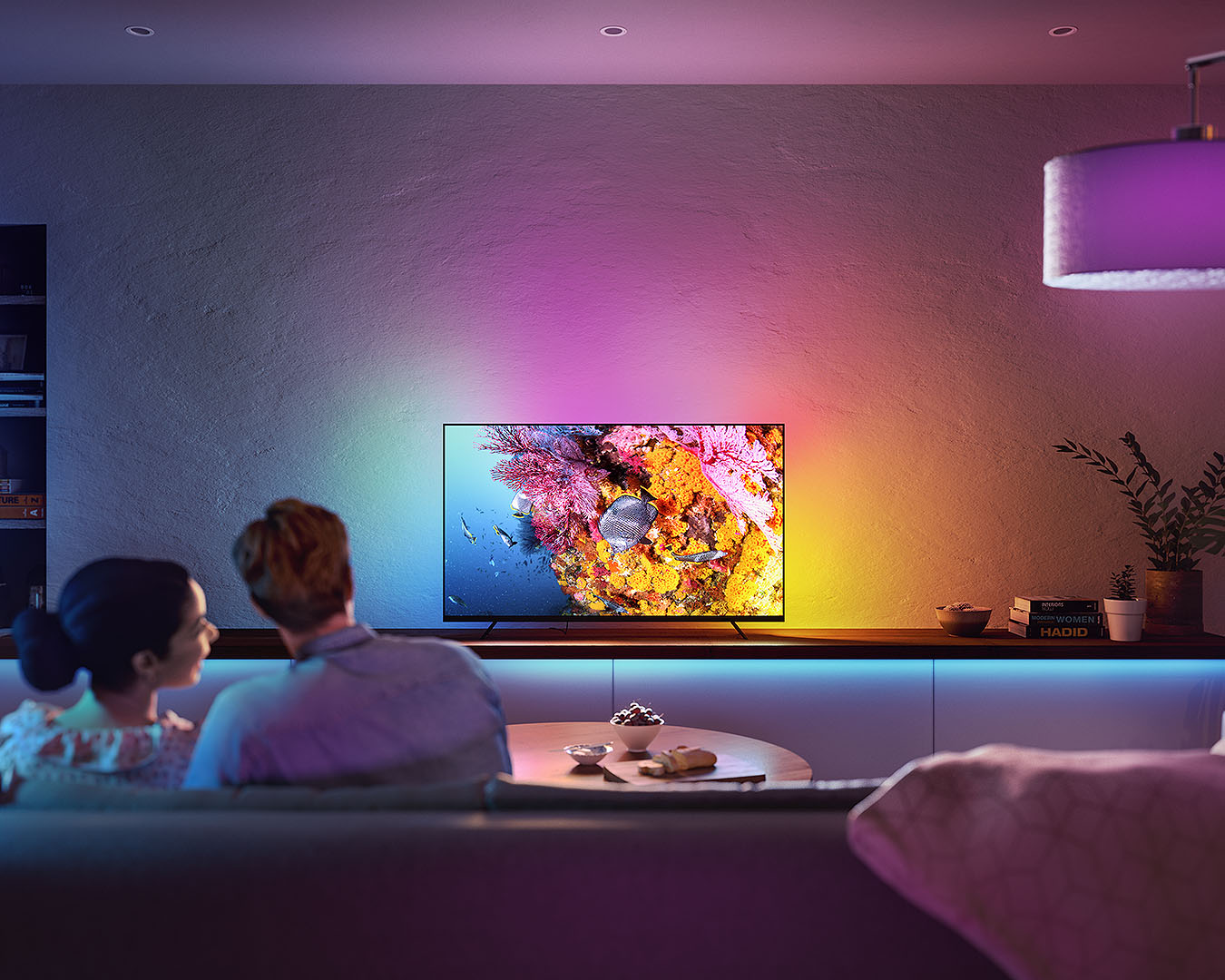 Two people sit in front of a colourful television set up.