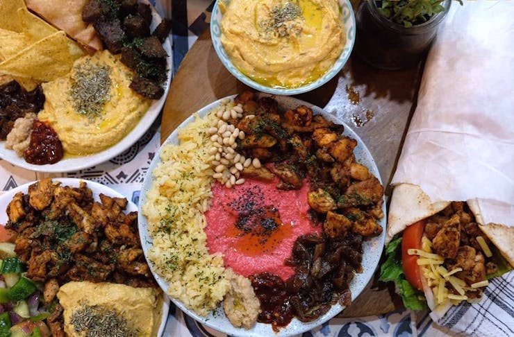 A table filled with a hummus platters, hummus bowls and a doner kebab.