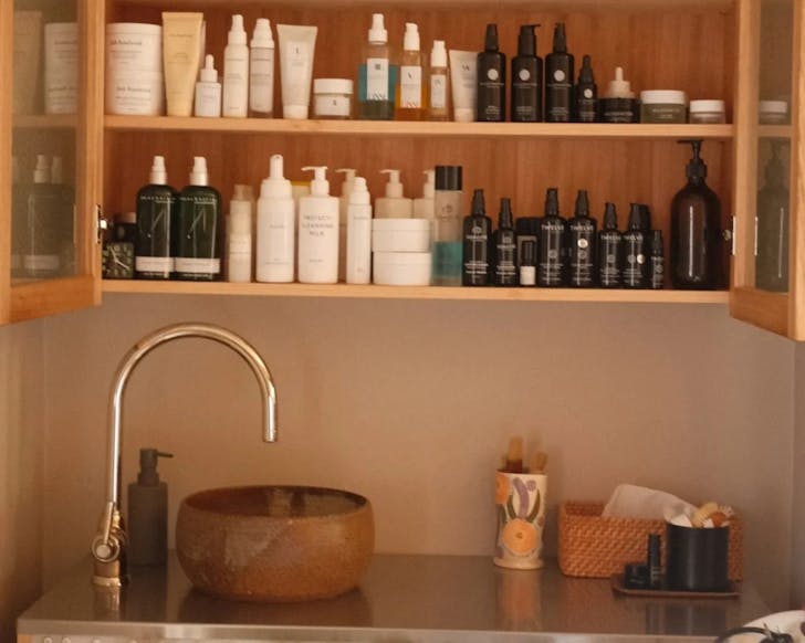 A clean sink with a wooden display cabinet above it, featuring rows and rows of skin-care and treatment products.