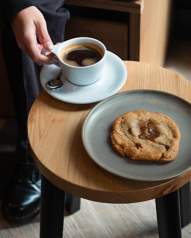 A black coffee in a white cup and a gooey-looking salted caramel cookie.