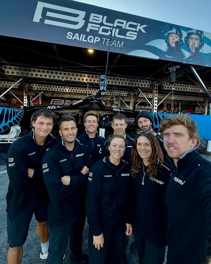 The SailGP NZ team pose in front of their dry-docked foil racing yacht.