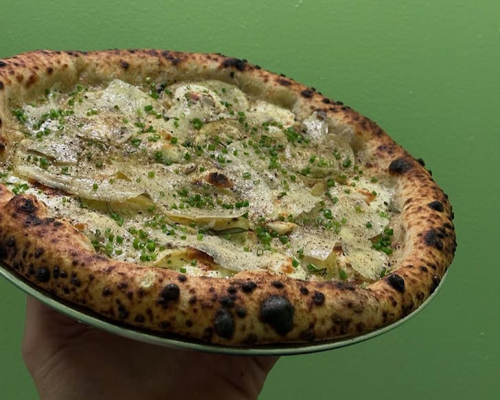 Lilliesâ signature woodfired pizza is held up against a green background 