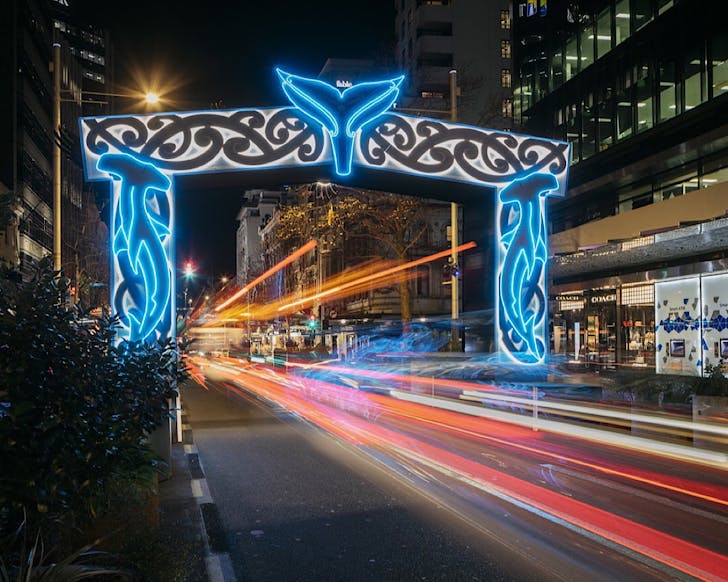 A neon-lit Te Wehenga Moana archwayâtraditional MÄori designs and a whale's tale in the middle archâabove a road in the city centre.