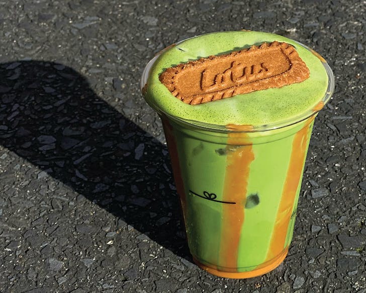 A cup of Thea matcha and biscoff milk is placed on the concrete from Blackdrop Cafe