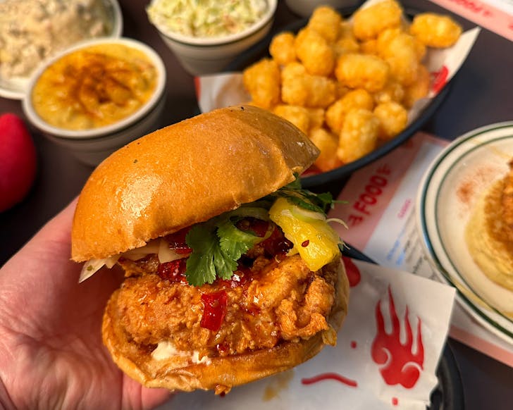 Vicki holds the Peachâs Hot Chicken and Door Dash NZ exclusive delivery only menu item, the Aloha Burger, in front of Peachâs signature sides