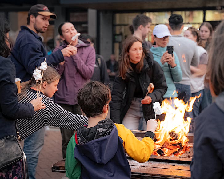 Families and couples gather around the open fire toasting their marshmallows for Åtautahiâs Fire On High Street Food Festival