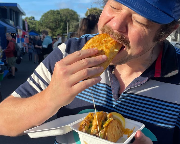 A happy customer bites into a fresh taco from Tacos El Carnal at Balmoral Street Food Market in TÄmaki