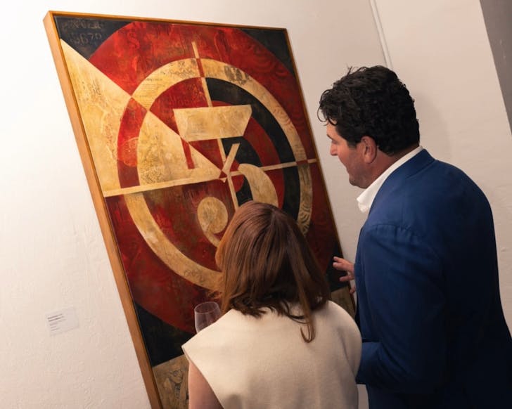The image is taken from behind as a man and women observe an Obey artwork hanging on the gallery wall.