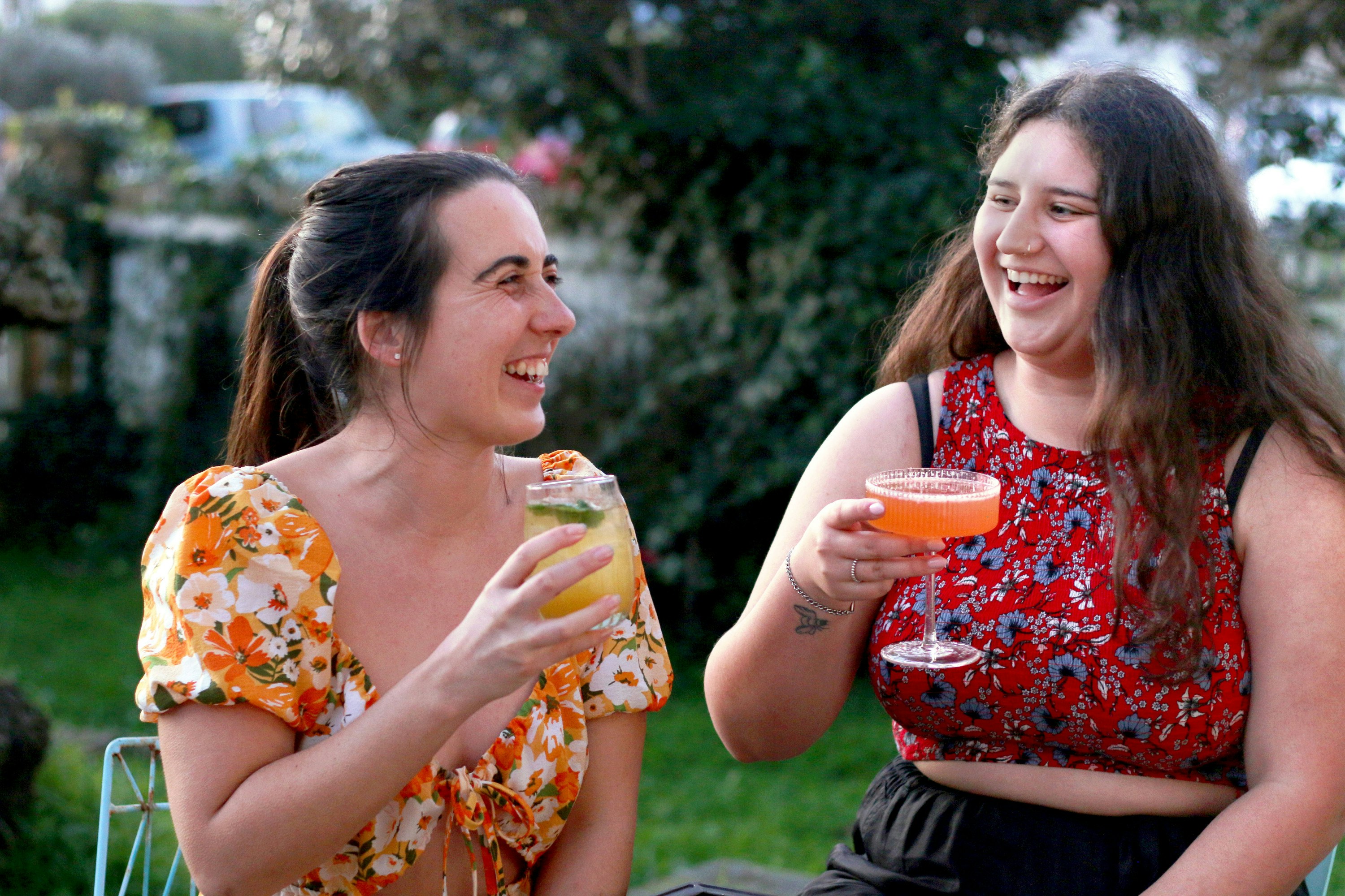 Two woman with cocktails smile.