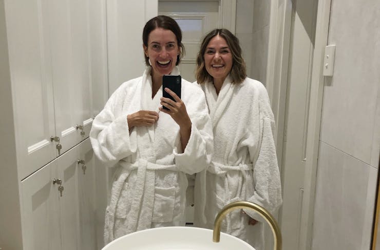 Two women in white robes take a selfie.