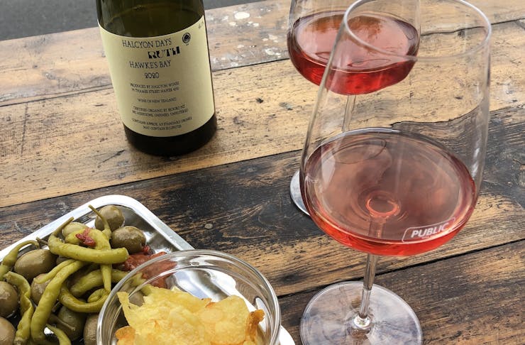 Two glasses of light red natural wine on a bar table with a platter of snacks.