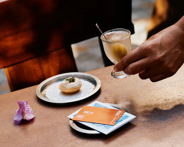 Person holding glass with card and tart on table below.