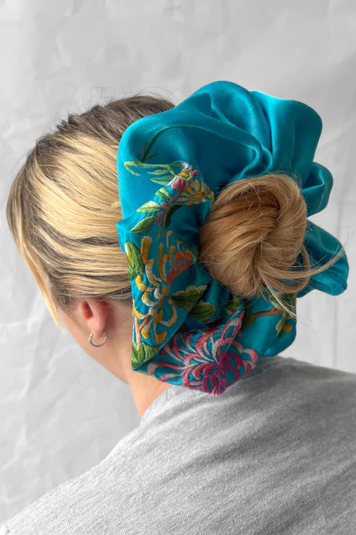 A blonde woman wears a giant scrunchy around her bun. 